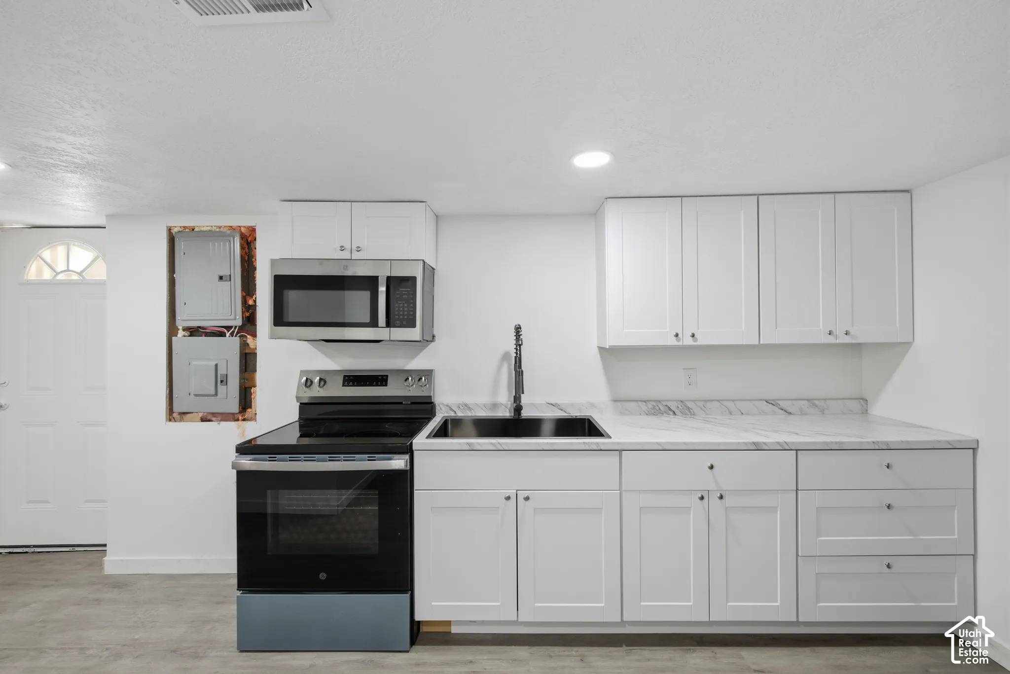 White shaker cabinetry, stone-finish countertops, stainless steel appliances, recessed lighting, and a modern black sink with a gooseneck faucet
