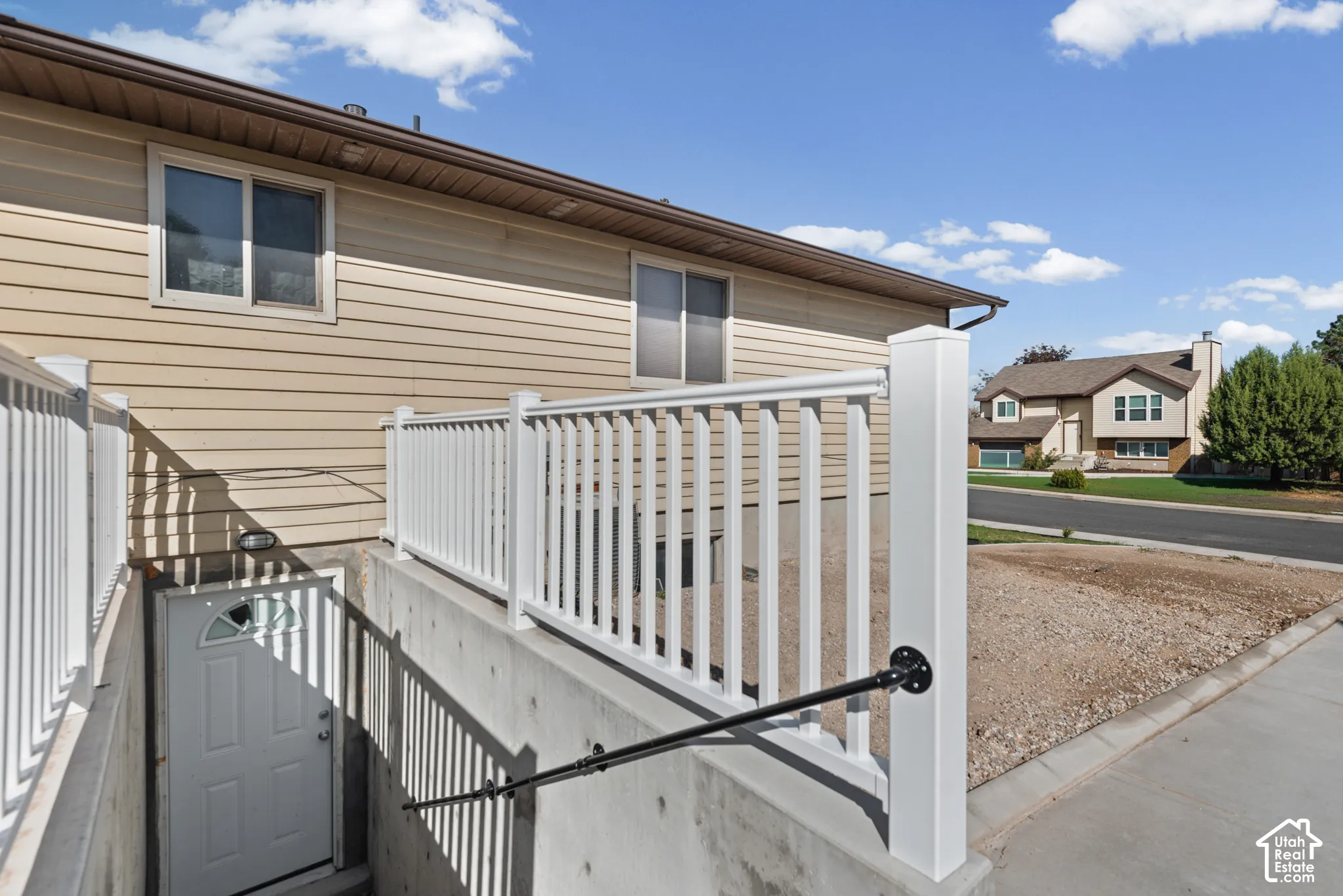 Exterior siding with multiple windows, concrete foundation, white railing, and a ground-level entry door