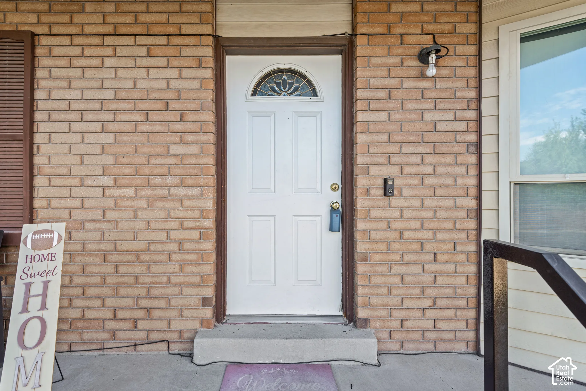 Brick exterior with a white entry door featuring an arched decorative glass insert and a security doorbell system