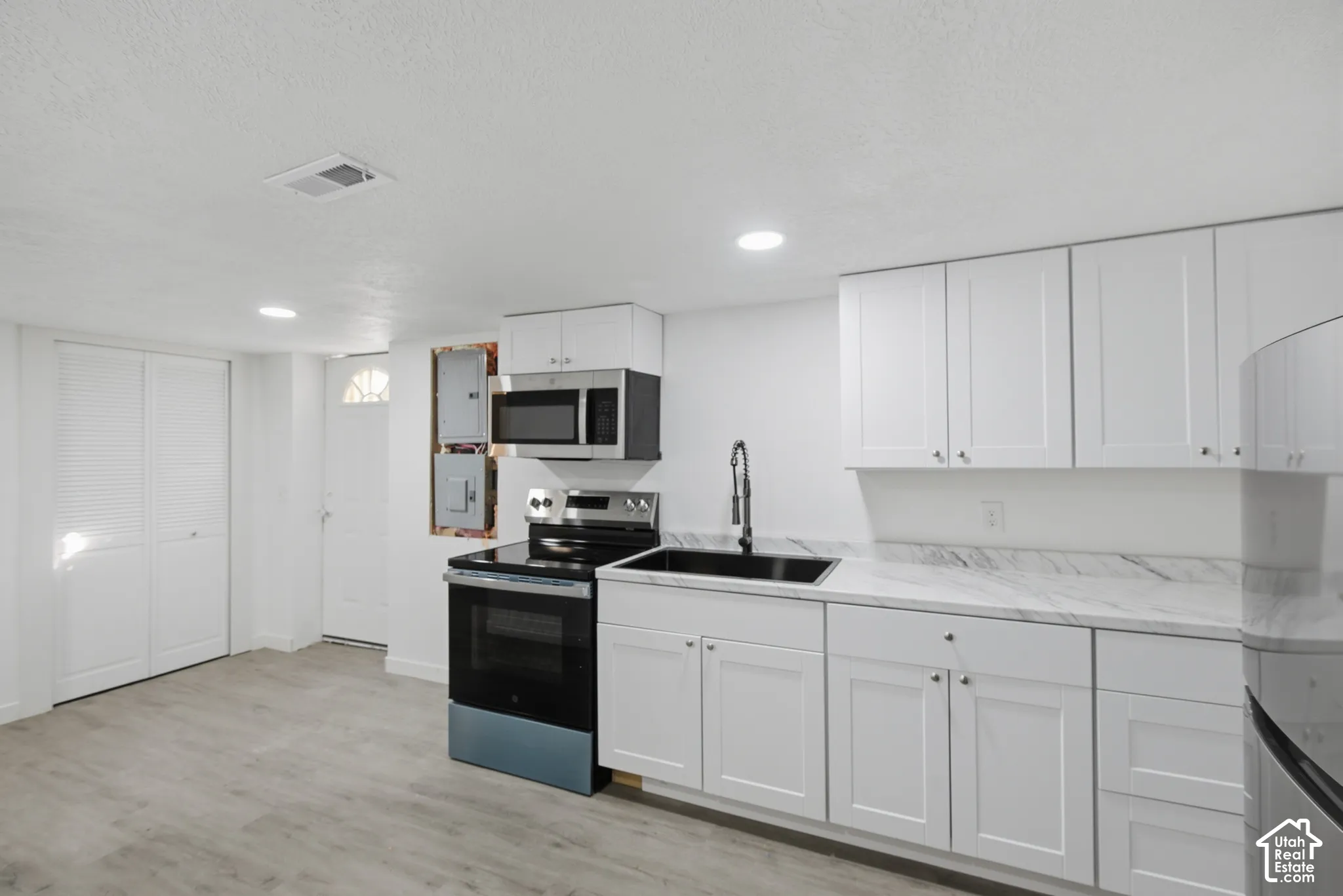 White cabinetry, integrated microwave, stainless steel range, black sink, and wood-finish flooring