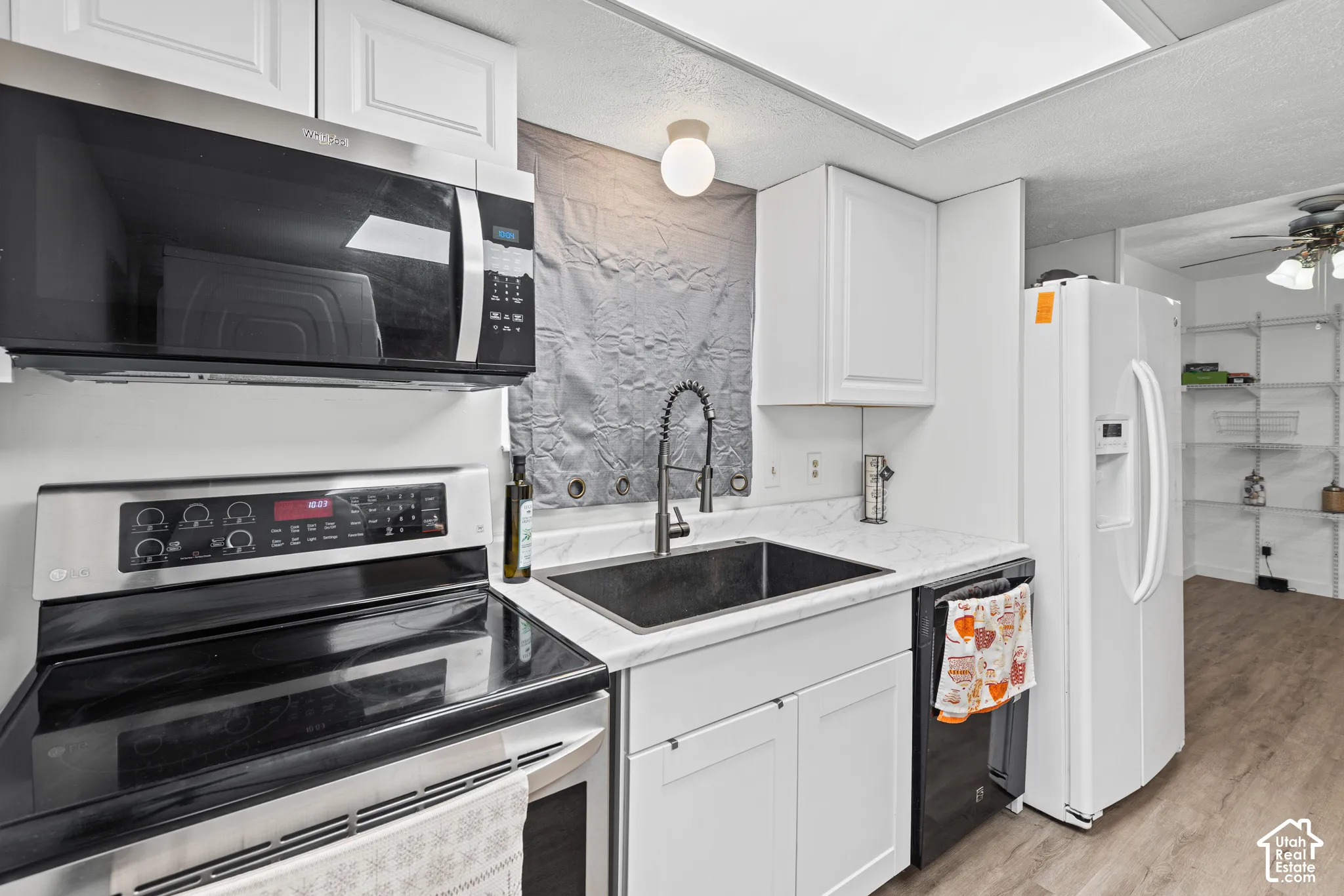 Kitchen featuring white cabinetry, stainless steel oven and microwave, dark sink with a gooseneck faucet, light-toned countertops, and wood-finish flooring