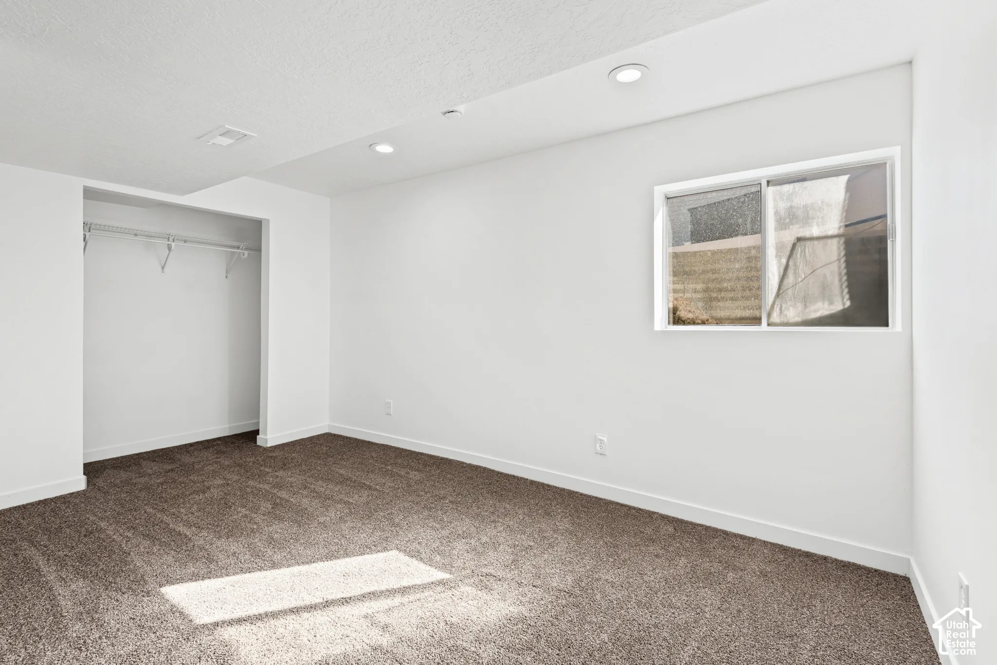 Carpeted flooring, recessed lighting, white walls, built-in closet with wire shelving, and a window
