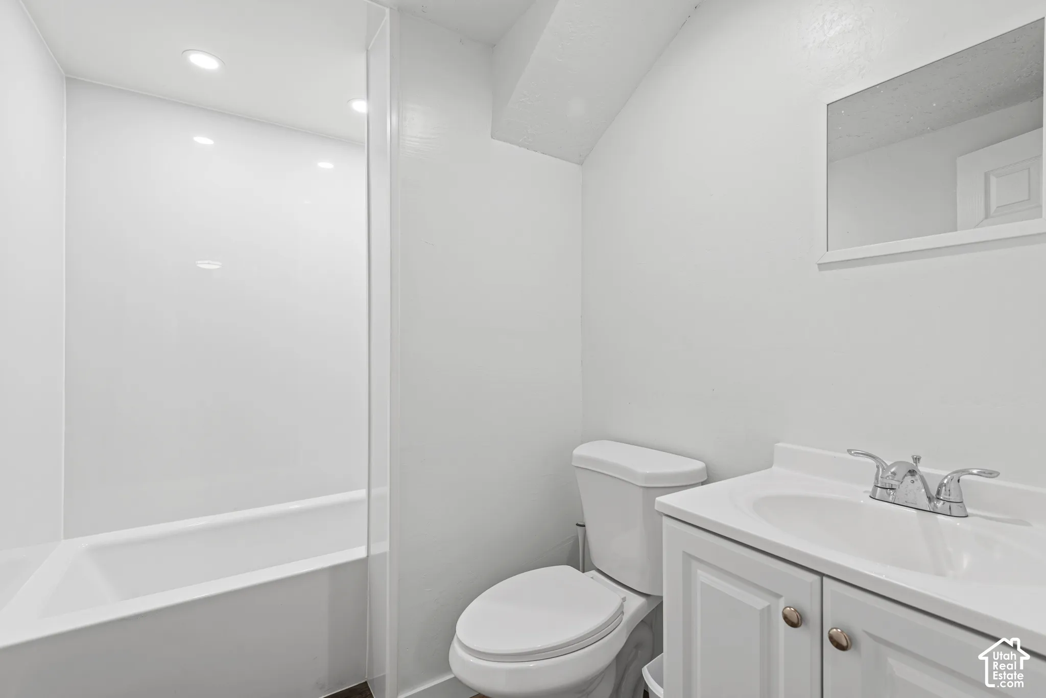 White bathroom featuring a built-in tub with a shower surround, a white toilet, and a vanity with a white sink