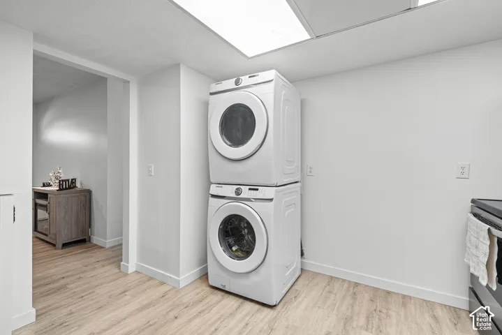 Stacked laundry appliances, overhead fluorescent lighting, wood-finish flooring, and white walls