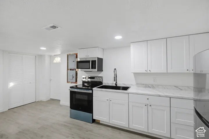 White cabinetry, integrated microwave, stainless steel range, black sink, and wood-finish flooring