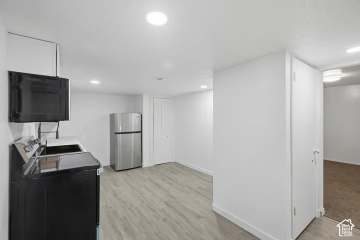 Recessed lighting throughout, light wood-finish flooring, stainless steel refrigerator, white walls, and a built-in microwave