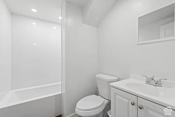 White bathroom featuring a built-in tub with a shower surround, a white toilet, and a vanity with a white sink
