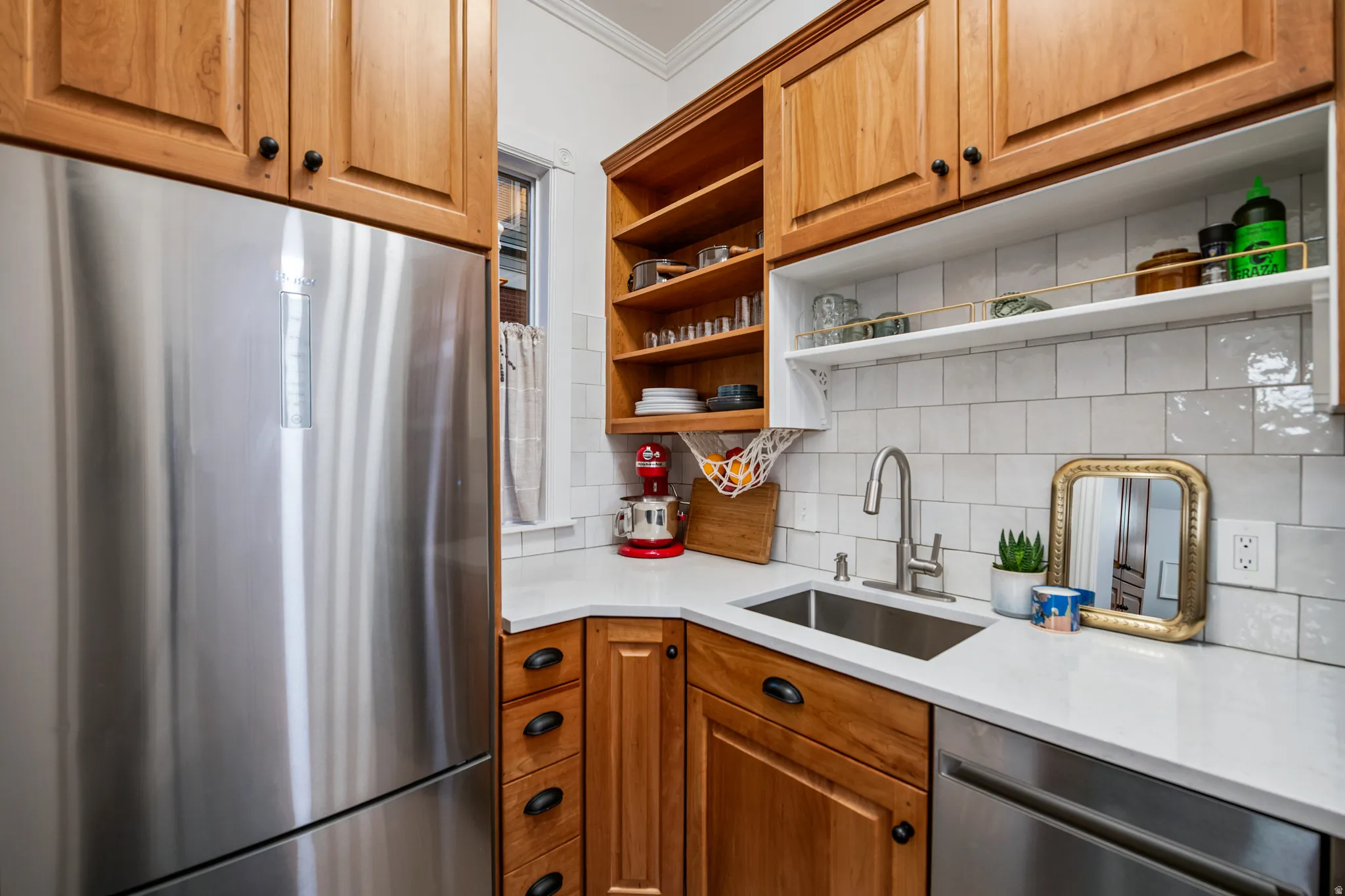 Stainless steel refrigerator, wood cabinetry, white subway tile backsplash, solid surface countertops, and an undermount sink with a gooseneck faucet