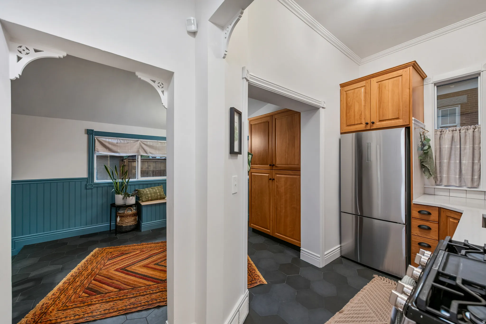 Decorative archway with corbel detailing, hexagonal floor tiling, wood cabinetry, built-in pantry, and a stainless steel refrigerator