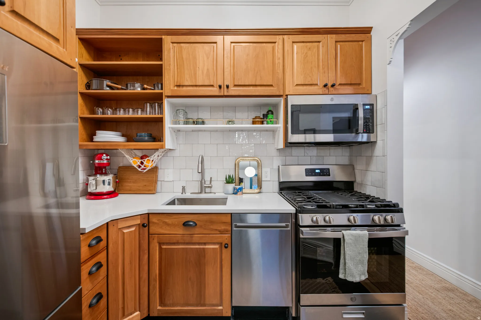Kitchen featuring wood cabinetry, stainless steel appliances, a single-basin sink, white subway tile backsplash, and light-toned countertops