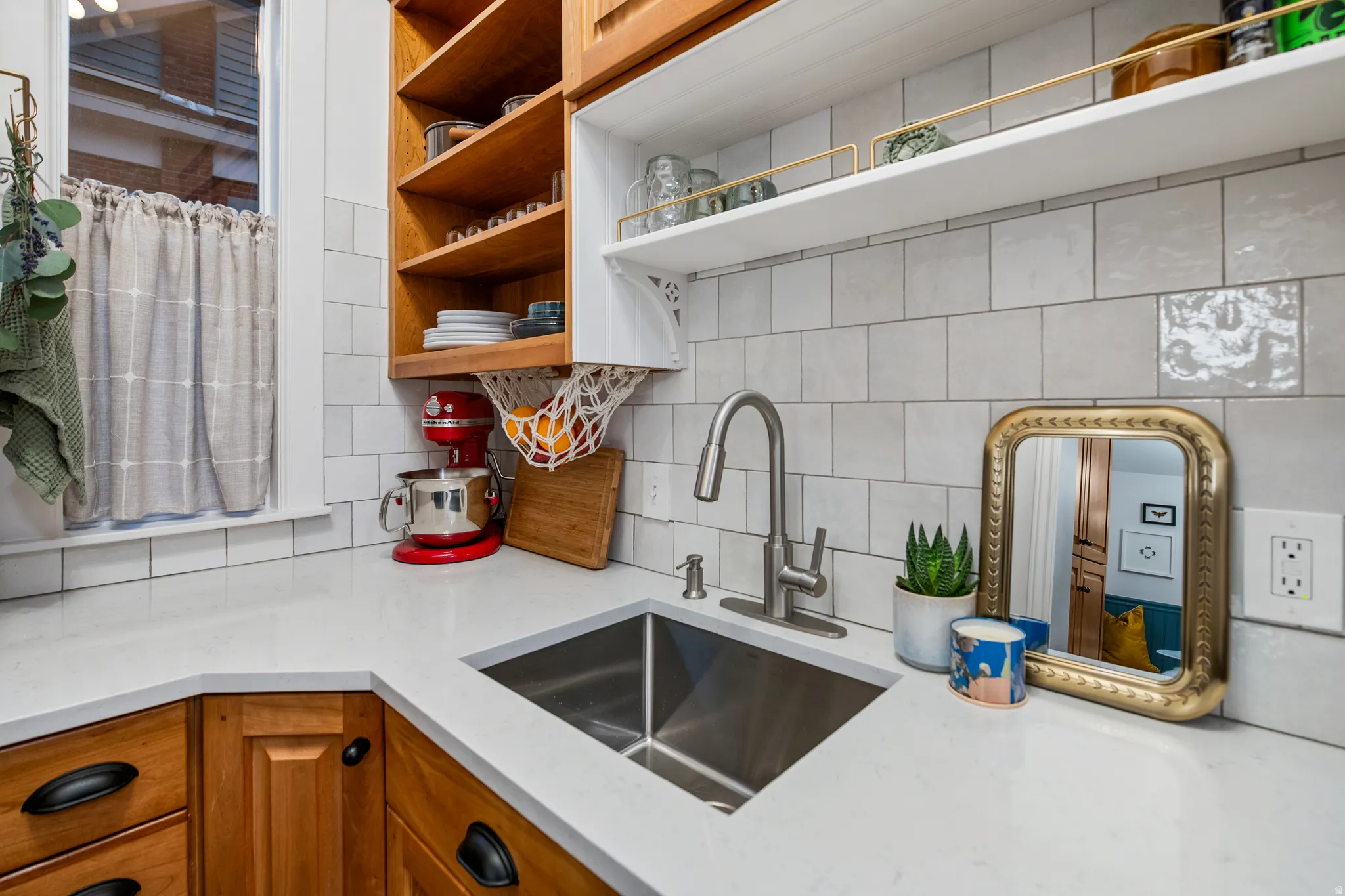 Corner sink with a stainless steel basin, a gooseneck faucet, light-toned countertops, subway tile backsplash, and wood-finish cabinetry with dark hardware