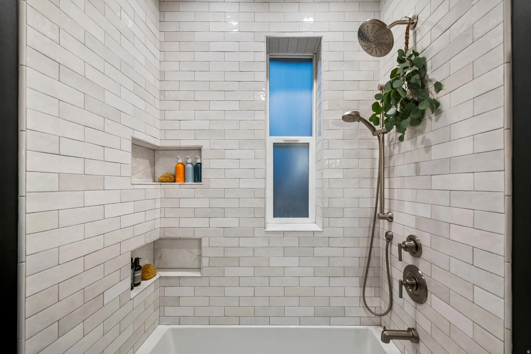 Subway tile shower surround featuring two recessed niches, a window, and brushed nickel fixtures