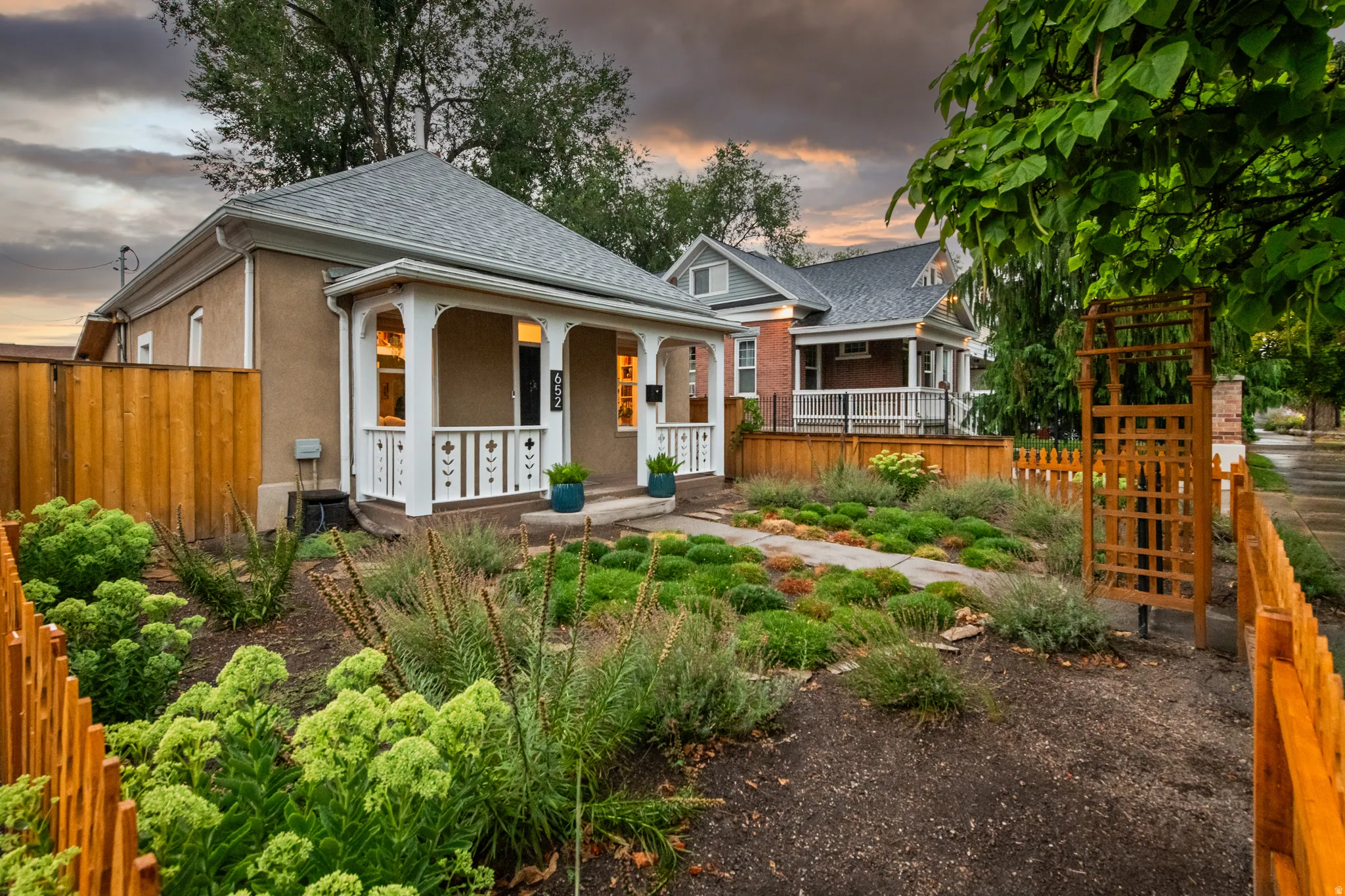 Stucco exterior with a covered porch, white decorative railings, and a gabled roof
