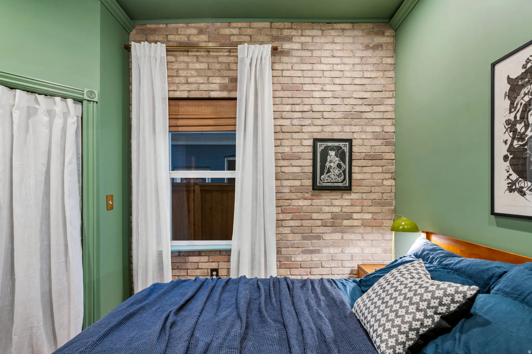 Exposed brick accent wall, double-hung window with wood-finish blinds, light green wall paint, coordinating green ceiling, and white curtains