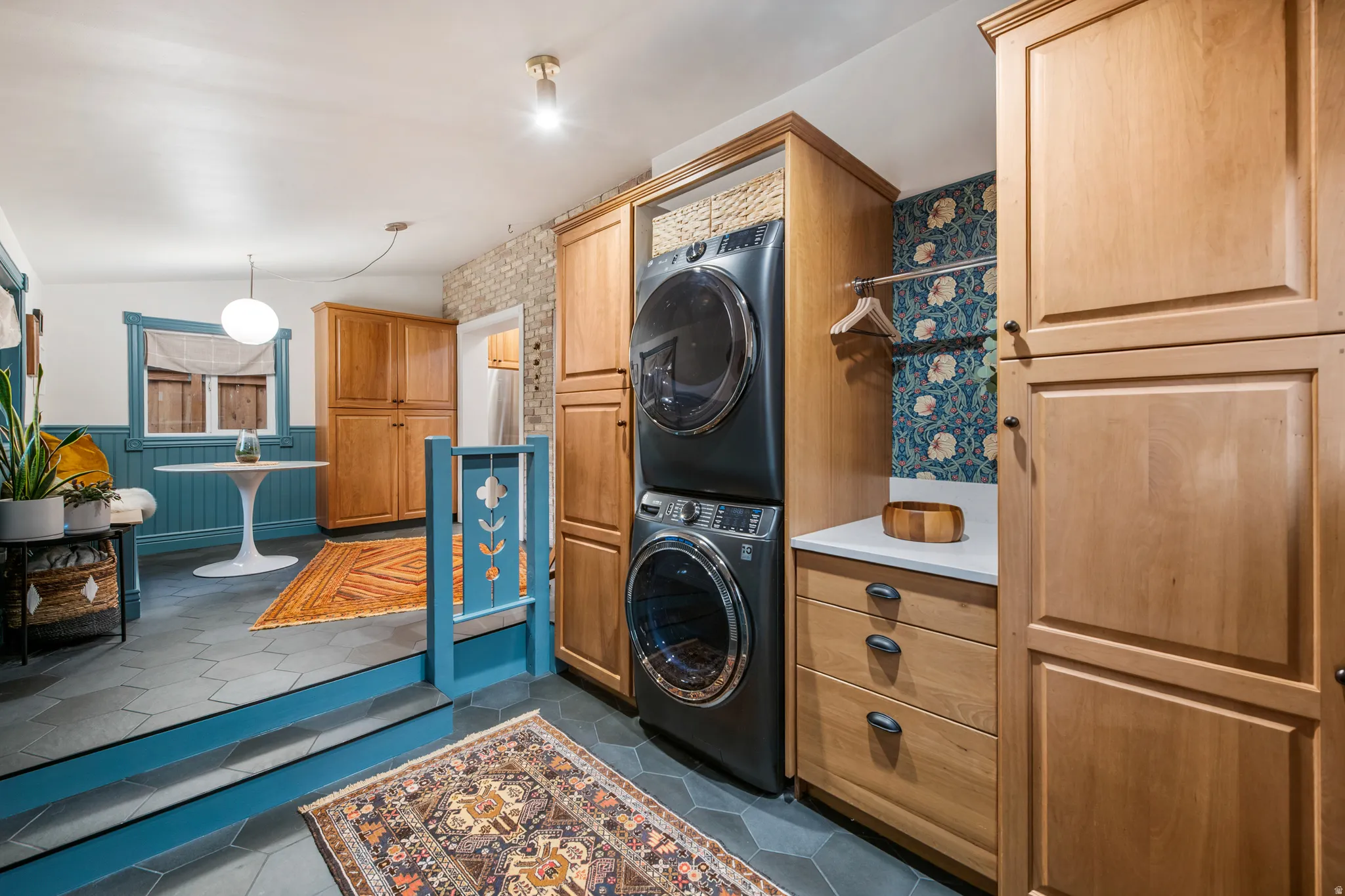 Stacked washer and dryer, wood cabinetry, white countertop, and hexagonal floor tiling