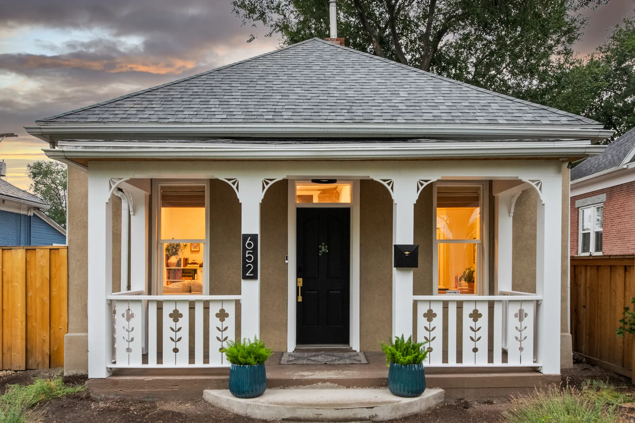 Gabled roofline, front porch with decorative railing, dark entry door, multiple front-facing windows, and a neutral exterior finish