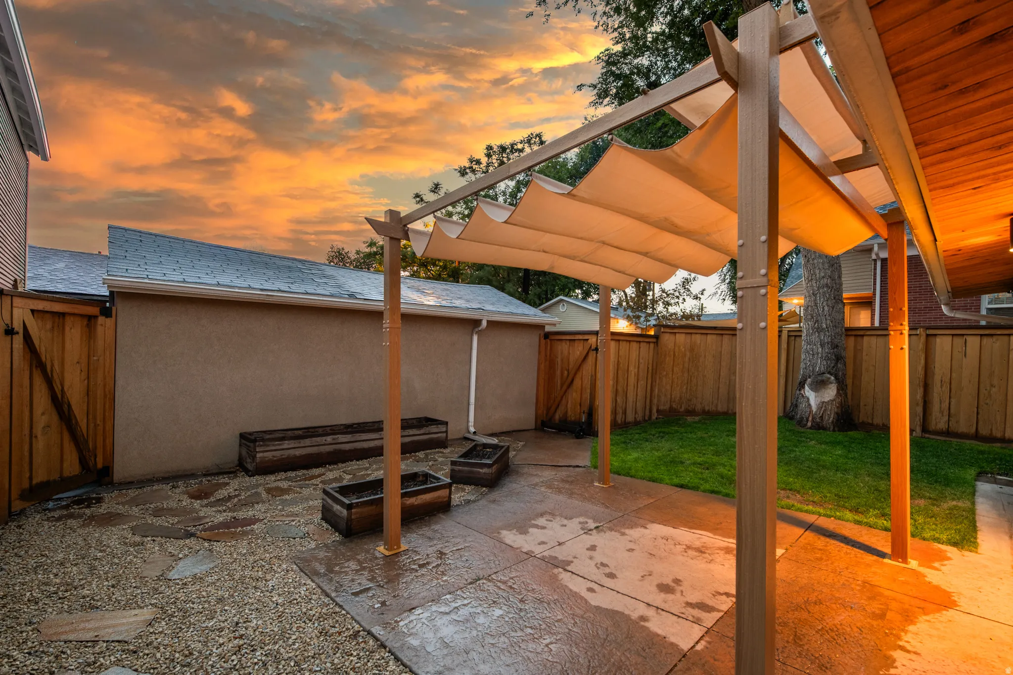 Outdoor living area featuring a retractable fabric pergola, stamped concrete patio, and a gravel-and-paver walkway