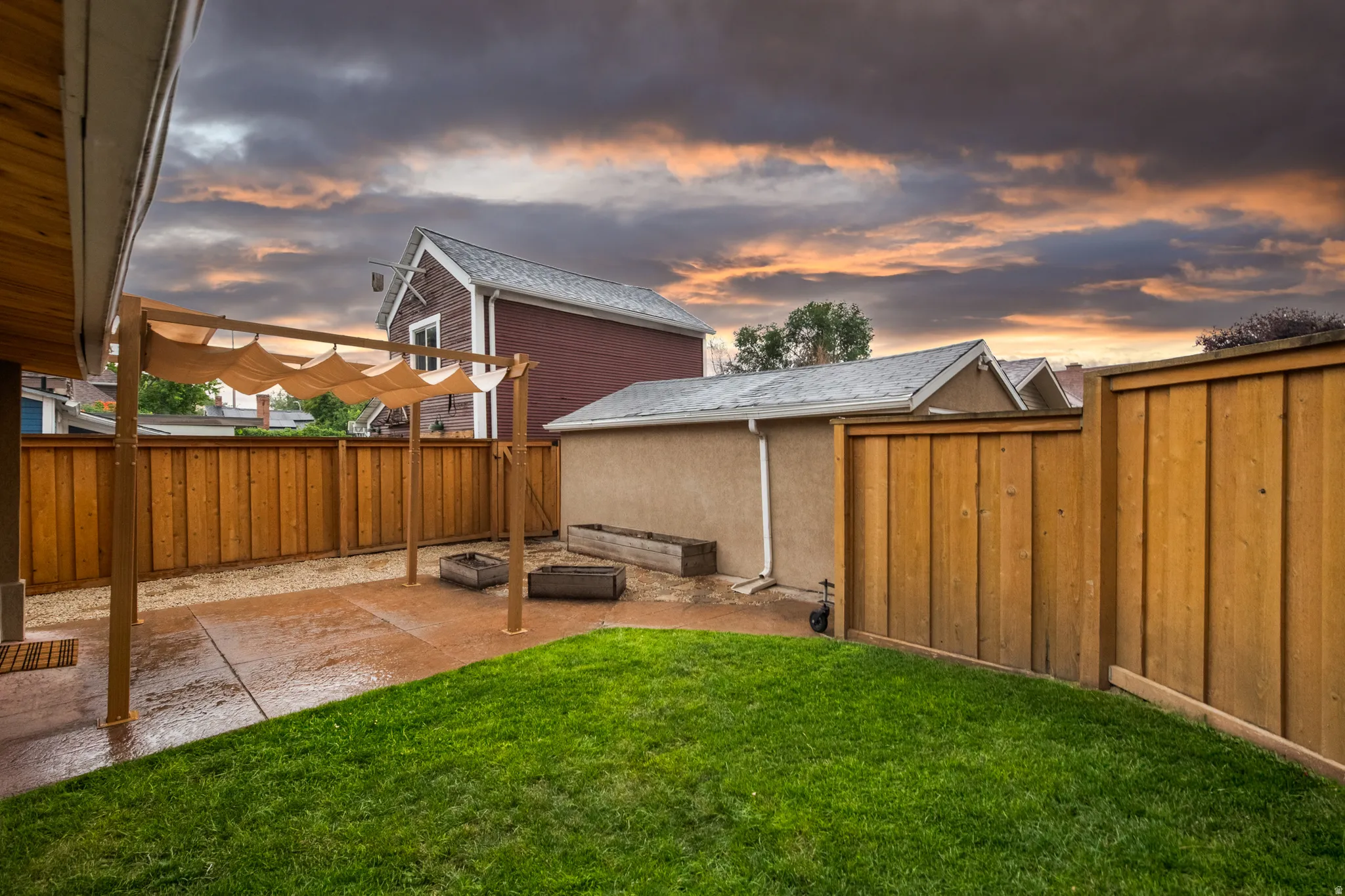 Expansive backyard featuring a wood-panel fence, green lawn, concrete patio, and a pergola with a fabric canopy