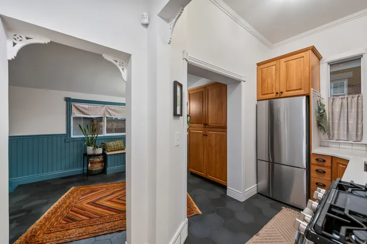 Decorative archway with corbel detailing, hexagonal floor tiling, wood cabinetry, built-in pantry, and a stainless steel refrigerator