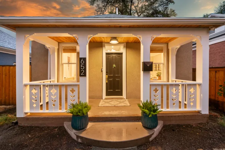 Covered front porch with decorative balusters, wood-finish ceiling, and sconce lighting
