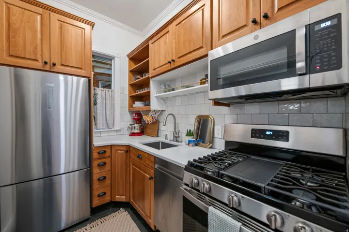 Stainless steel appliances, wood cabinetry, built-in shelving, white subway tile backsplash, and light-toned countertops