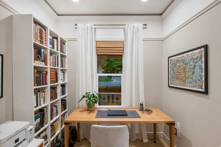 Built-in shelving, crown molding, recessed lighting, wood-finish flooring, and a large window with window treatments