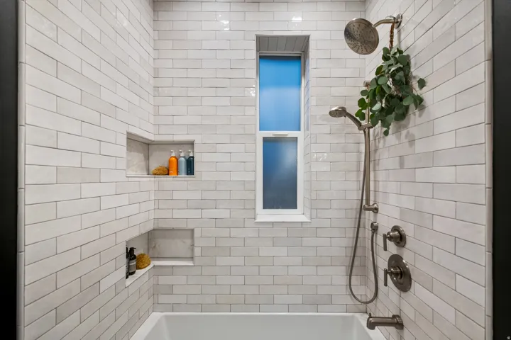 Subway tile shower surround featuring two recessed niches, a window, and brushed nickel fixtures