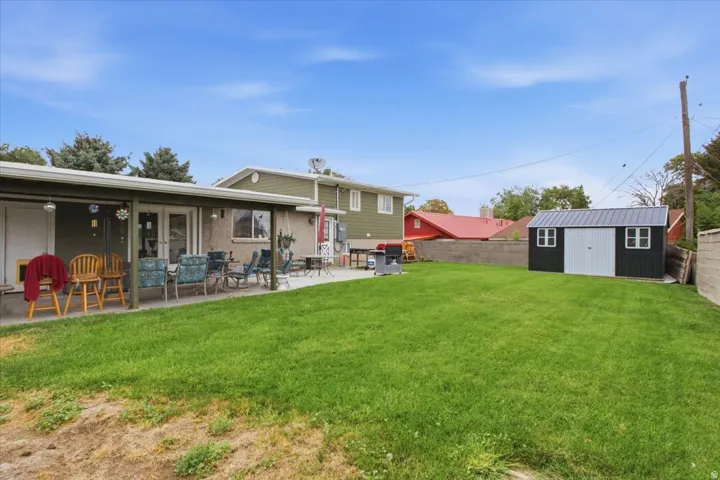 Expansive grassy yard featuring a covered patio, concrete patio, and a storage shed.