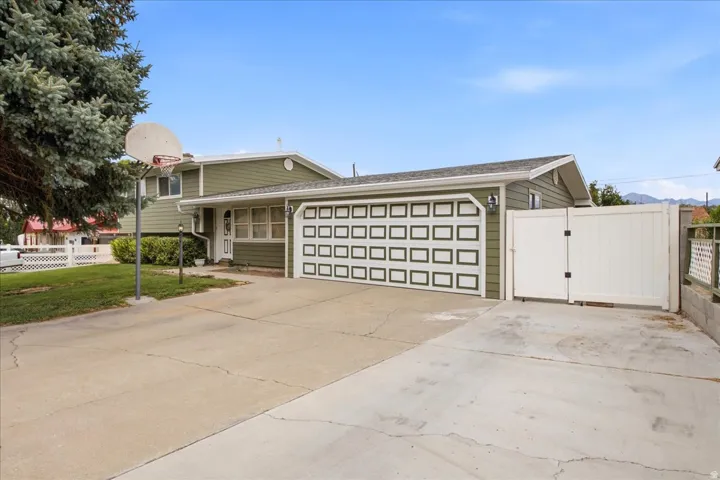 Siding exterior with an attached two-car garage featuring a paneled door, a white privacy fence, and a concrete driveway