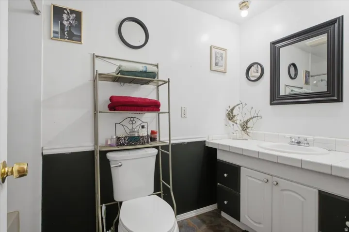 Bathroom with a white toilet, dark base cabinets, white upper cabinets, and a white tile countertop