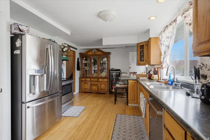 Kitchen with wood-finish flooring, stainless steel appliances, wood cabinetry, dual basin sink, and recessed lighting