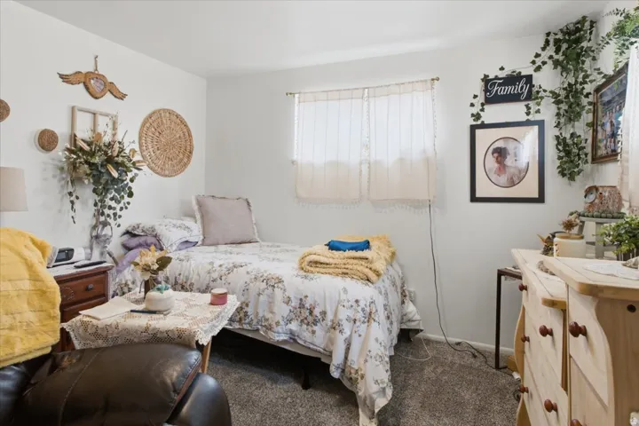 Wall-to-wall carpeting with a bright window, wood-finish nightstand.