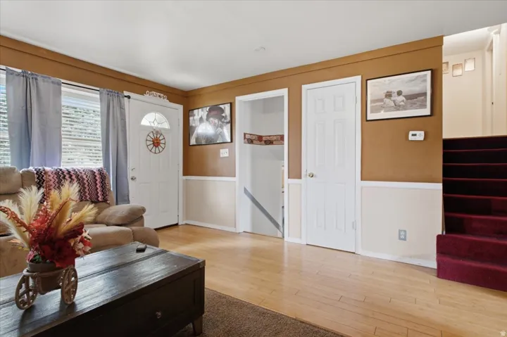Hardwood-finish flooring, white paneled door, partial wall paneling, and a carpeted staircase