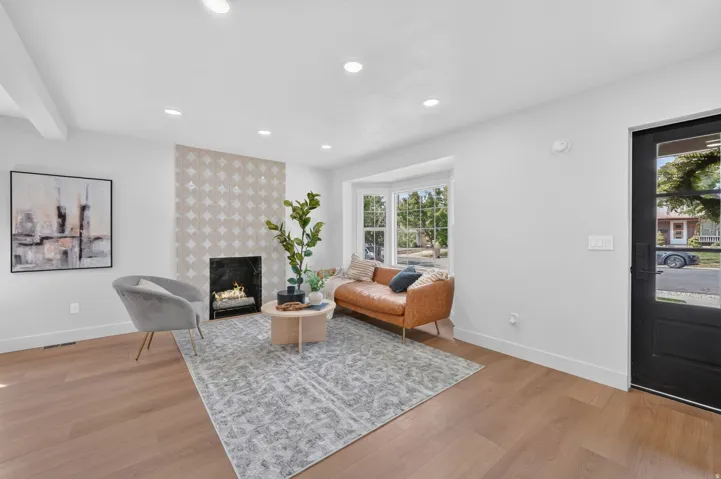 Wood-finish flooring throughout, bay window with multiple panes, recessed ceiling lighting, and a fireplace with a decorative tile surround and black hearth