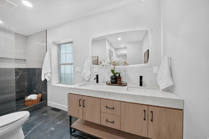 Dual vanity with light wood-finish cabinetry, integrated sinks, and matte black fixtures