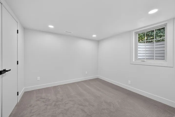 Recessed lighting illuminates a space featuring gray wall-to-wall carpeting and white baseboards