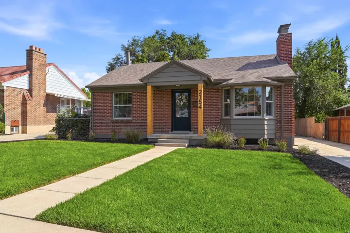 Brick exterior with a gabled entry, a bay window, a concrete pathway, a shingled roof, and a manicured lawn