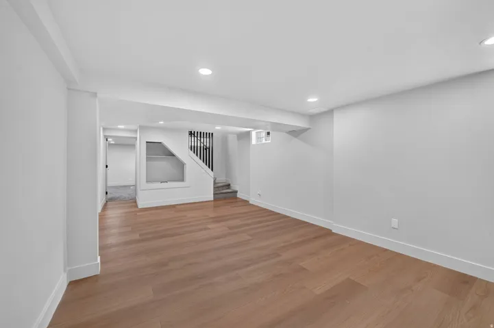 Recessed lighting, wood-finish flooring, white walls, built-in shelving, and a black wrought iron stair railing