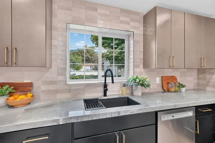 Kitchen featuring light gray upper cabinetry with gold-toned hardware, black lower cabinetry, a black sink with a matte black faucet, and a stainless steel dishwasher