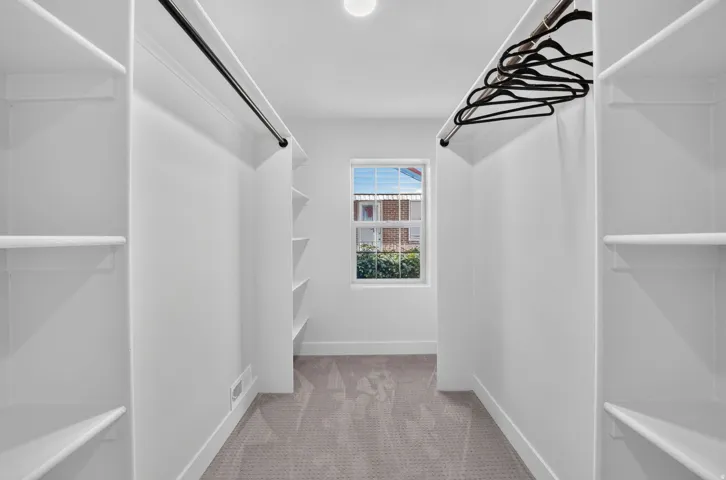 Walk-in closet featuring white built-in shelving, hanging rods, and a window for natural light