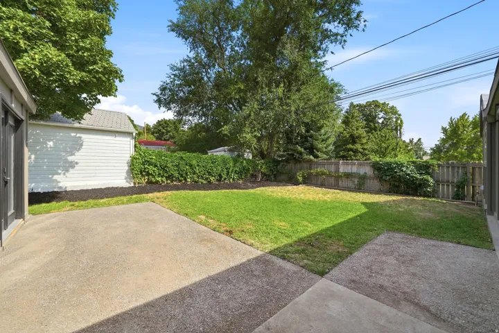 Expansive backyard featuring a concrete patio, a manicured lawn, a wooden privacy fence, and mature trees