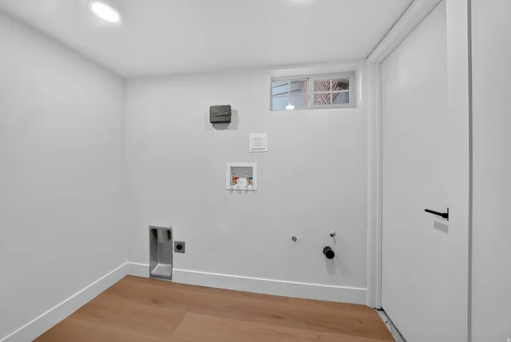 Utility space featuring wood-finish flooring, recessed lighting, and a white paneled door with a black lever handle