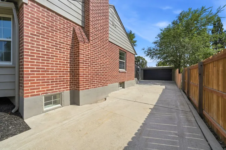 Brick exterior with a prominent chimney feature, basement window, concrete driveway, and a wood privacy fence