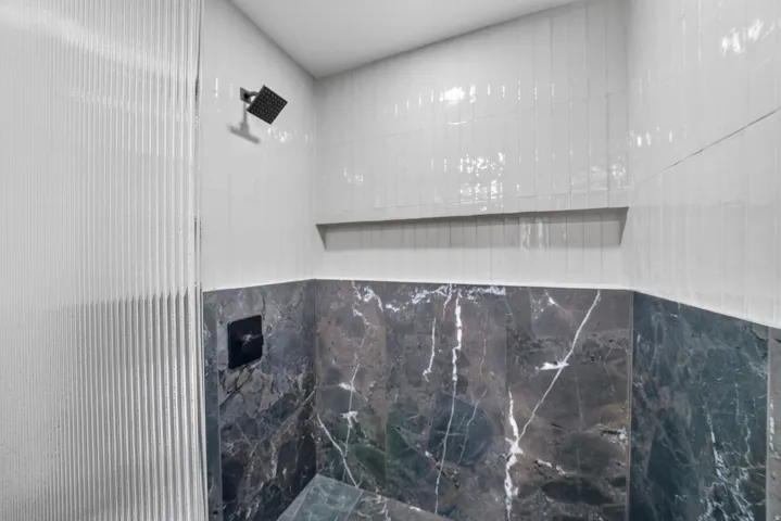 White vertical subway tile, dark veined tile, matte black shower head, and matte black shower controls