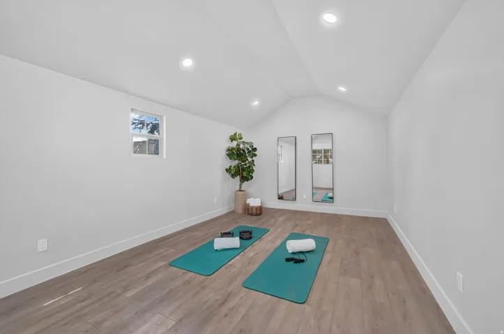 Vaulted ceilings with recessed lighting, wood-finish flooring, and a window
