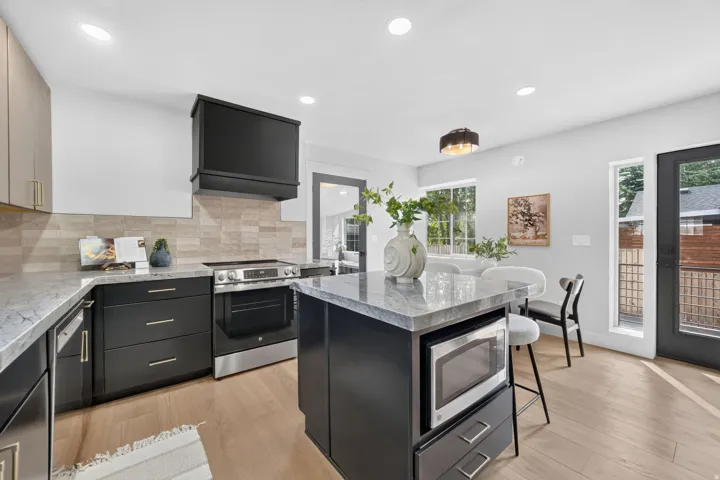 Modern kitchen featuring wood-finish flooring, stainless steel appliances, a kitchen island with seating, dark cabinetry, and light-toned countertops