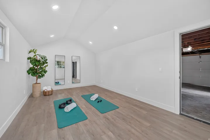 Vaulted ceiling with recessed lighting, wood-finish flooring, white walls, and a window
