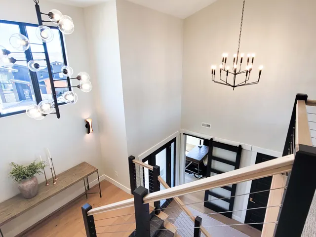 High ceilings with contemporary chandeliers, wood-finish flooring, modern staircase with cable railing, and a barn door entry