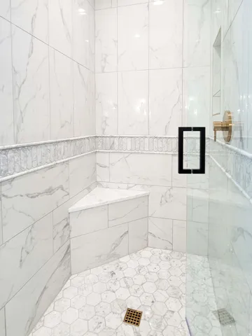 Walk-in shower with full-height wall tiling, mosaic accent band, built-in corner bench, and hexagonal floor tiling