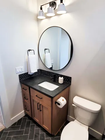 Wood-finish vanity with an integrated sink, dark countertop, and black hexagonal tile backsplash